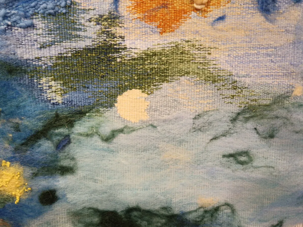 Detail in which woven tapestry dissolves into felted wool: blues and greens, a pale disc, a flare of orange.
